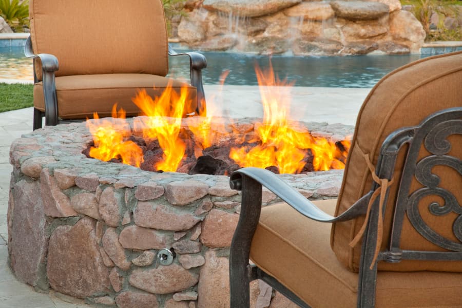 Outdoor fire pit made with stone veneer situated next to in-ground pool