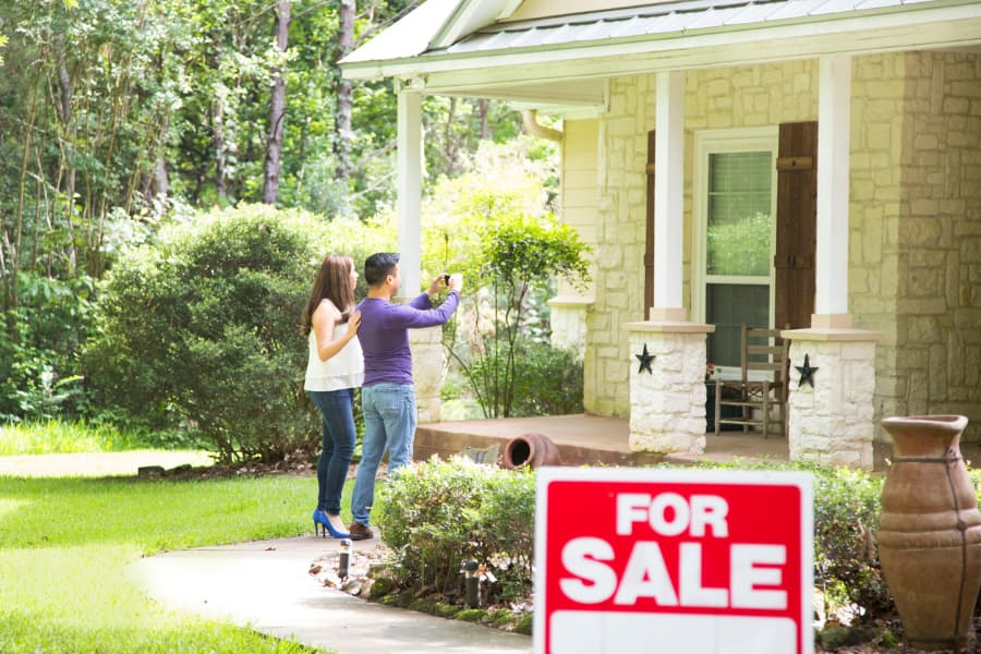 Potential home owners taking image of a house with a for sale yard sign