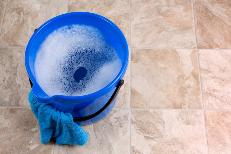 Blue plastic bucket filled with warm water and dish soap creating soapy solution